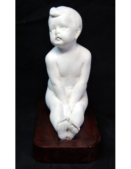 Figura de niño desnudo sentado.